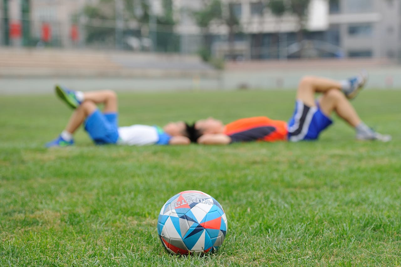 services-01 Two teenagers lying on grass near a soccer ball, enjoying leisure time outdoors.